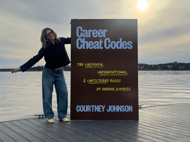 Courtney Johnson posing beside a large outdoor display of her book Career Cheat Codes on a waterfront dock at sunset